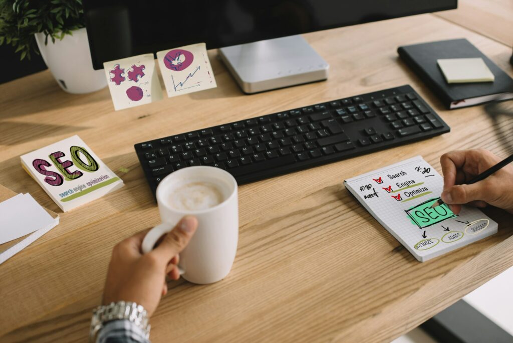 cropped shot of seo manager writing notes with cup of coffee and computer at workplace